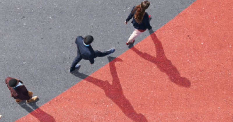 Three people walking from a bird's eye view, on grey and red flooring, with long shadows on the red surface.
