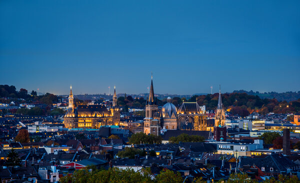 Abendliche Stadtansicht von Aachen mit beleuchtetem Aachener Dom und historischen Gebäuden.