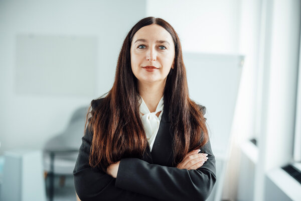 A portrait photograph of a smartly dressed woman wearing a white blouse and black blazer, with her arms crossed.