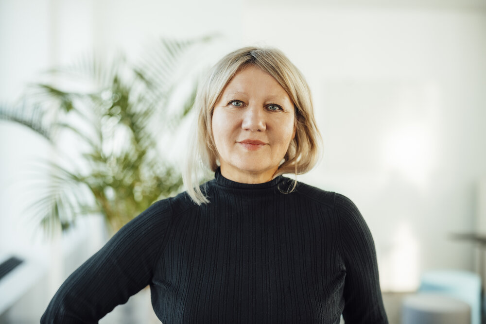 A portrait photograph of a woman in an office wearing a black jumper.