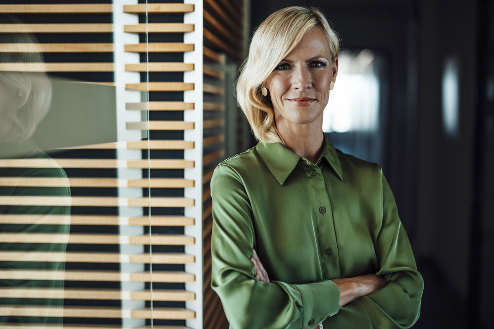 A portrait photograph of a woman wearing a green velvety blouse and crossing her arms.