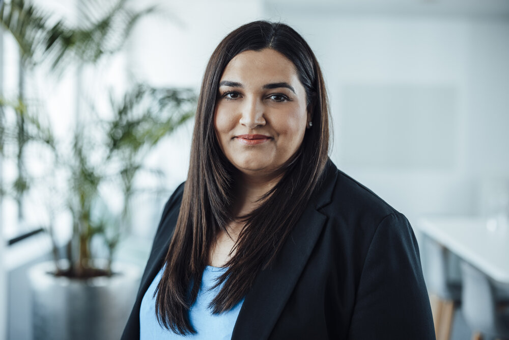 A portrait photograph of a woman standing sideways to the camera and wearing a black blazer.