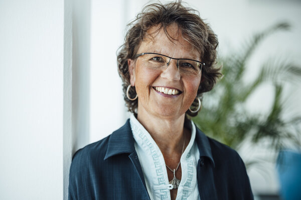 A portrait photograph of a woman. She is standing sideways against an office wall and smiling at the camera.