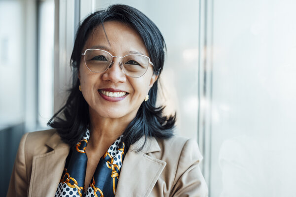 A portrait photograph of a smartly dressed woman wearing glasses and a scarf decorated with various motifs.