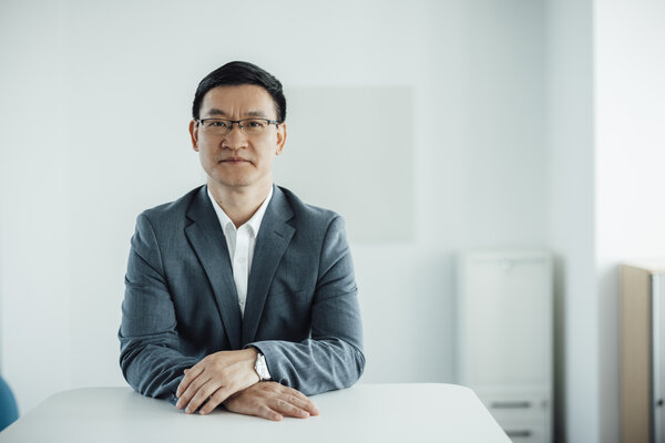 A portrait photograph of a smartly dressed man sitting behind an office desk with his hands resting on it.