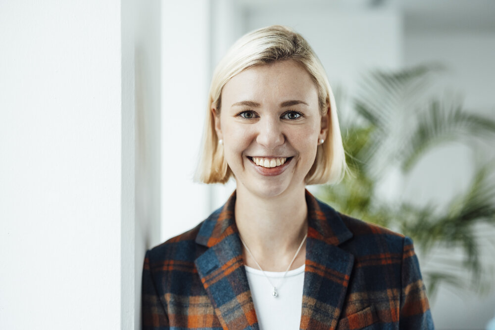 A portrait photograph of a young woman wearing a white shirt, a checked blazer and a silver necklace.