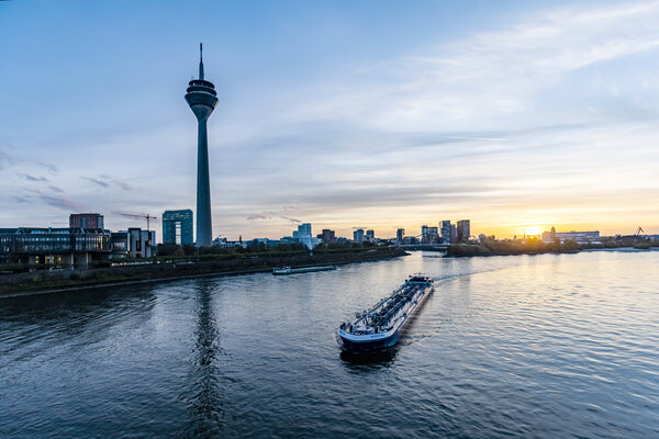 A view of the Rhine with a passing ship, television tower and Düsseldorf skyline at sunset.