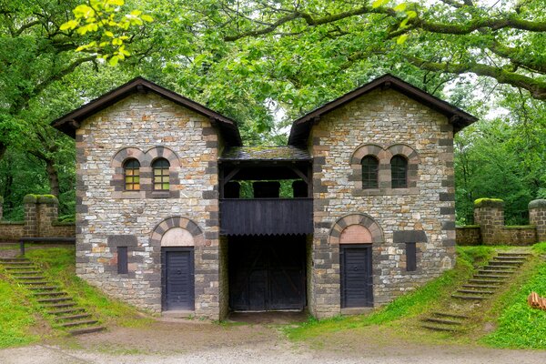 Der steinerne Torbau des Niedergermanischen Limes mit zwei Türmen und Rundbogenfenstern, flankiert von Treppenaufgängen und alten Bäumen.