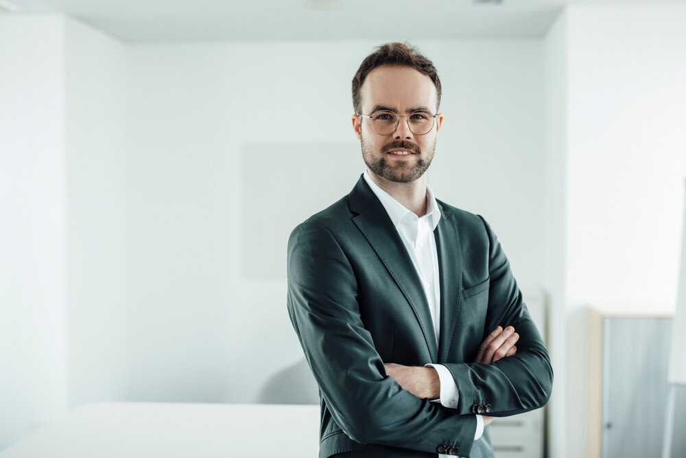 A portrait photo of a young man in a white shirt and black jacket. He has his arms crossed.