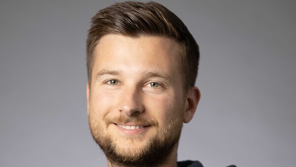 A portrait photograph of a young man wearing a hoodie and with styled brown-blond hair. 