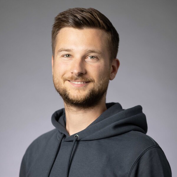 A portrait photograph of a young man wearing a hoodie and with styled brown-blond hair. 