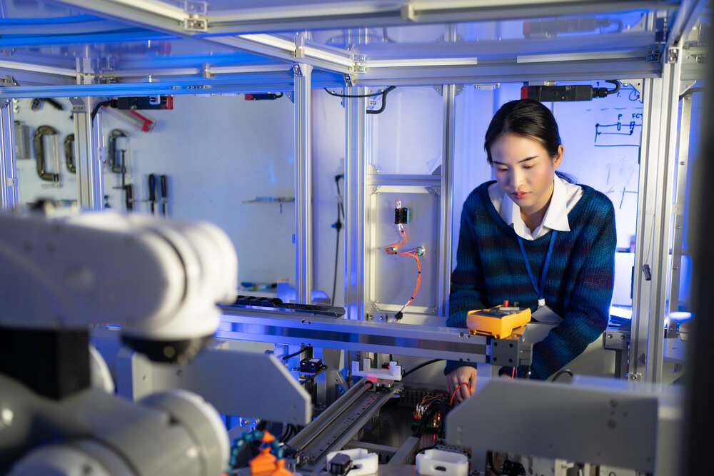A woman in a laboratory at an automated machine with a robotic arm and other electronic components.