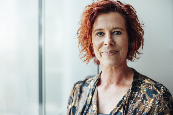 A portrait photograph of a woman in an office wearing a blouse with various patterns. 