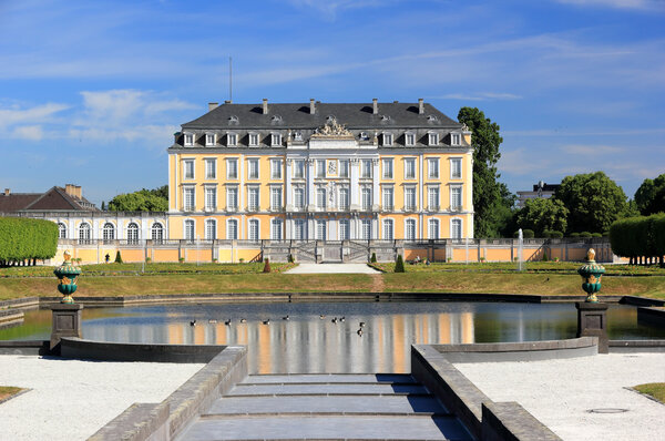 Prunkvolles Schloss Augustburg mit gelber Fassade und vielen weißen Fenstern, davor ein Garten mit Wasserbecken, Treppen und Vasen.