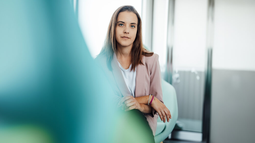 A portrait photograph of a smartly dressed young woman sitting on a chair.