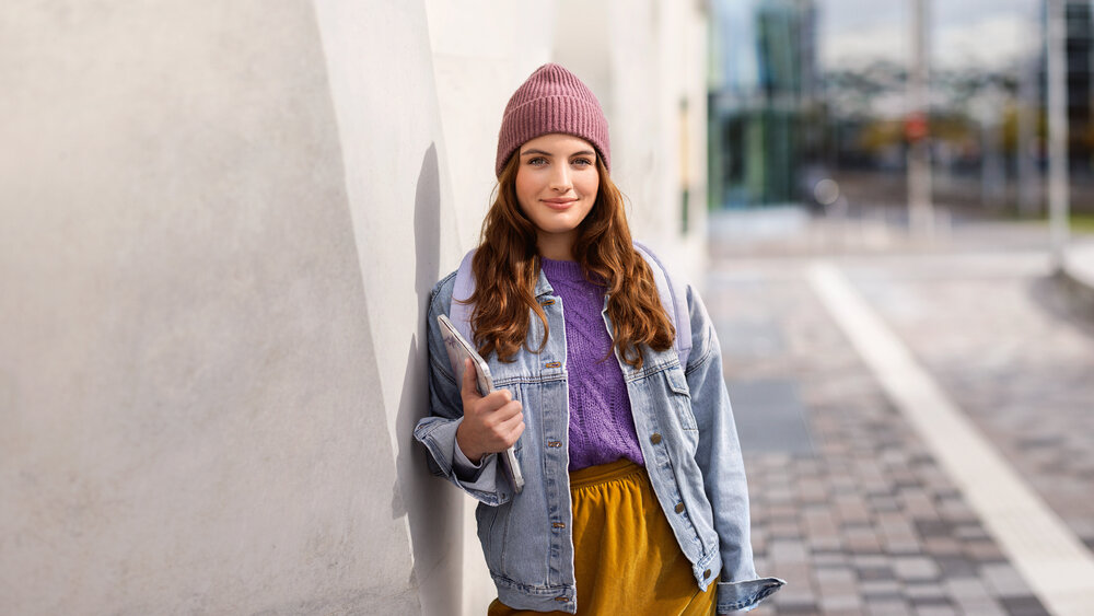 Young woman leaning against a light-colored wall holding a tablet