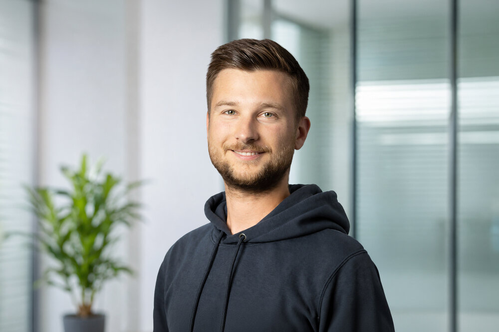 A portrait photograph of a young man wearing a hoodie and with styled brown-blond hair. 