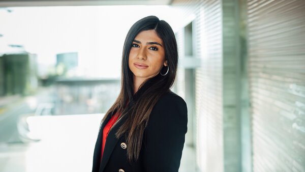 A portrait photograph of a woman wearing a black blazer. She is standing sideways to the camera.