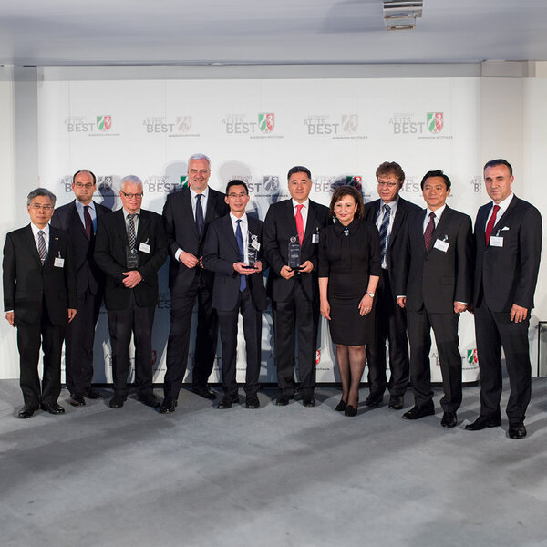 Eleven people in business attire stand side by side, three holding glass trophies, with a screen in the background displaying the words “Germany at its best”.