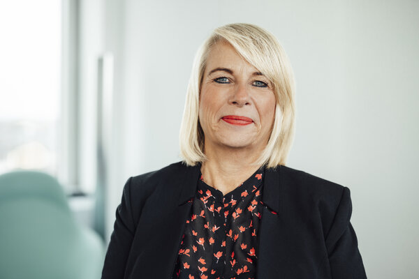 A portrait photograph of a woman wearing a black blouse with red patterns and a blazer.