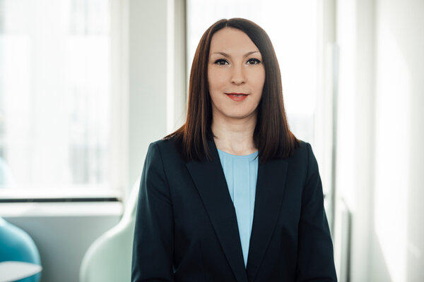 A portrait photograph of a young woman wearing a light blue blouse and a dark navy blue blazer.