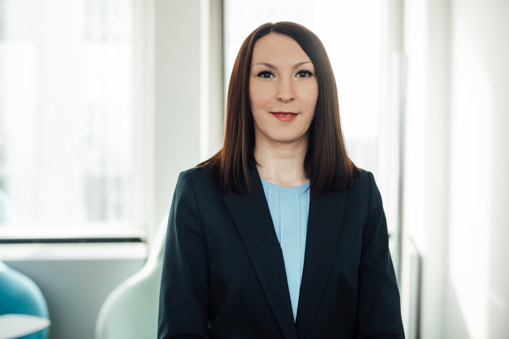 A portrait photograph of a young woman wearing a light blue blouse and a dark navy blue blazer.