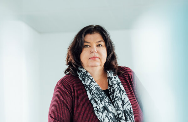 A portrait photograph of a woman sitting behind an office desk wearing a black and white patterned scarf.