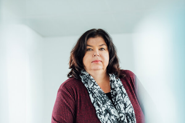A portrait photograph of a woman sitting behind an office desk wearing a black and white patterned scarf.