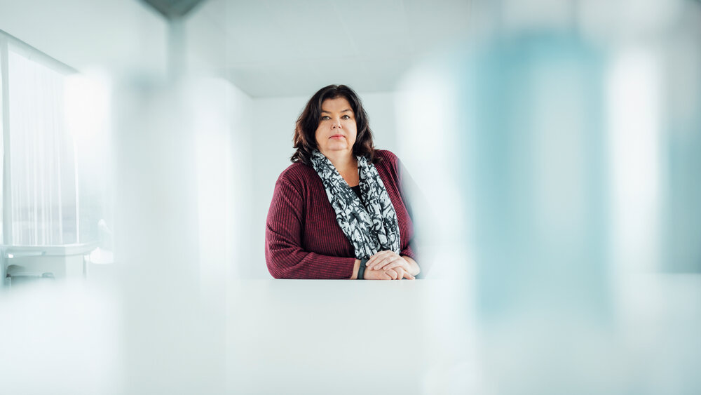 A portrait photograph of a woman sitting behind an office desk wearing a black and white patterned scarf.