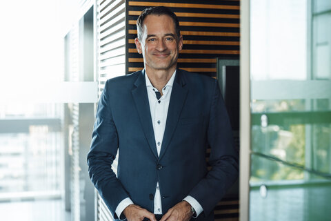 A portrait photograph of a smartly dressed man wearing a white shirt and a dark navy blue jacket.