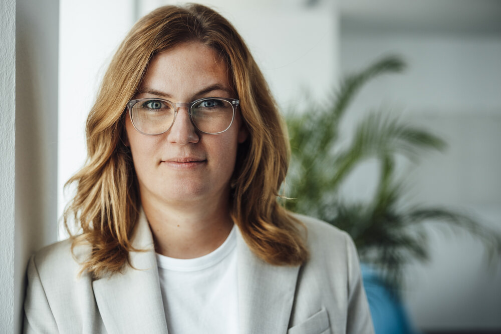 A portrait photograph of a woman wearing glasses and a light grey blazer.