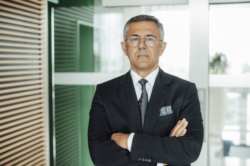 A portrait photograph of a smartly dressed man with his arms crossed in front of a glass partition.