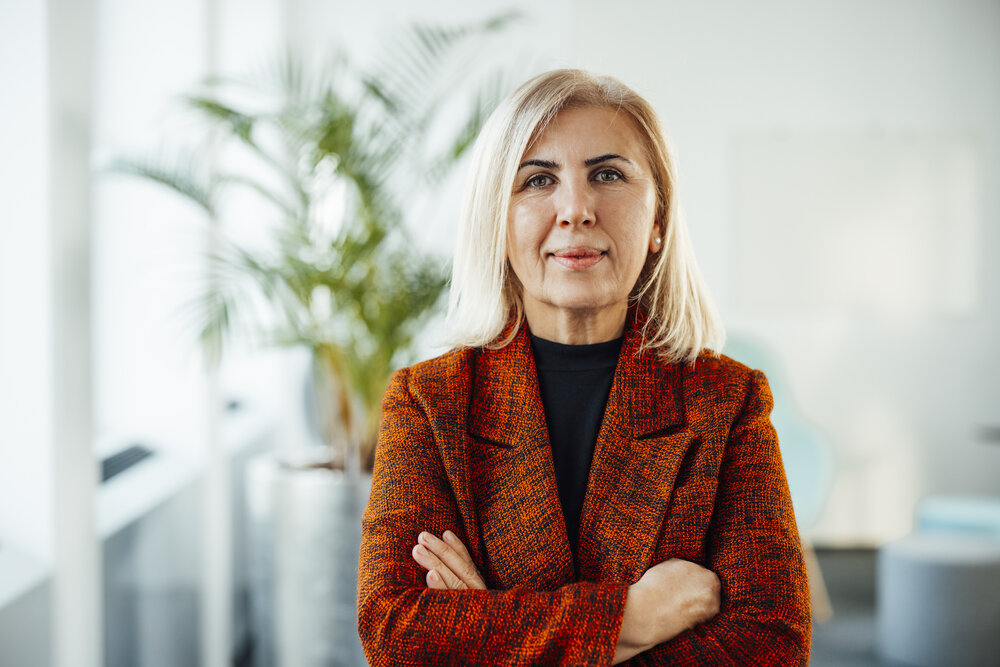 A portrait photograph of a smartly dressed woman in a black and orange blazer with her arms crossed.
